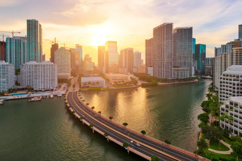 Miami skyline and waterfront at sunset, with a bridge crossing Biscayne Bay